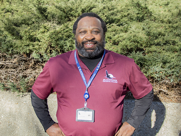 Will, a bearded man in a maroon BTC polo, stands in th sunshine of BTCs Central Campus Courtyard