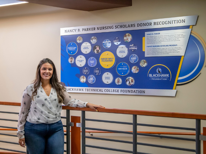 Lorena Hebble, former student and scholarship recipient, in front of donor wall