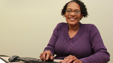 Woman typing at keyboard smiling at camera