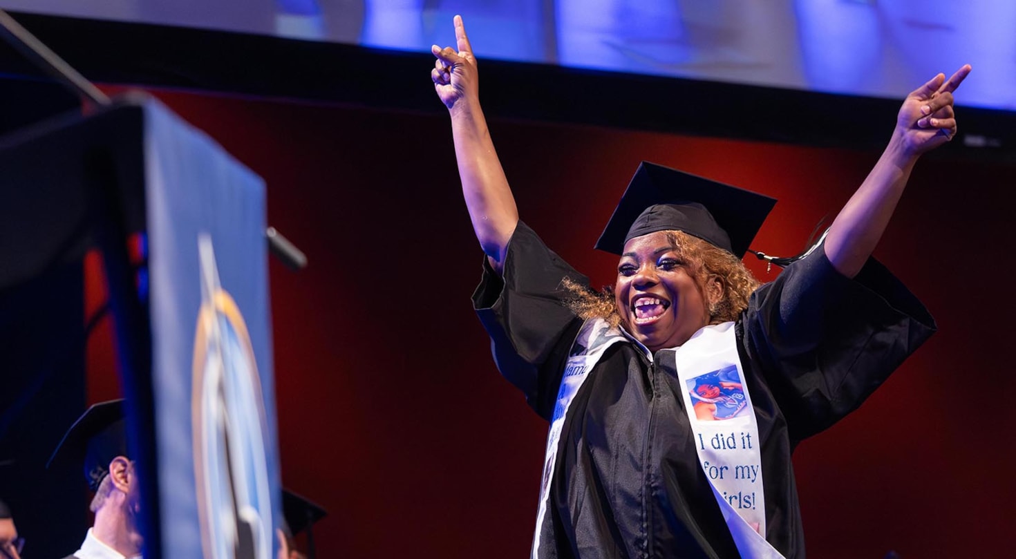 Female graduate in graduation gown and cap celebrating with her arms in the air 