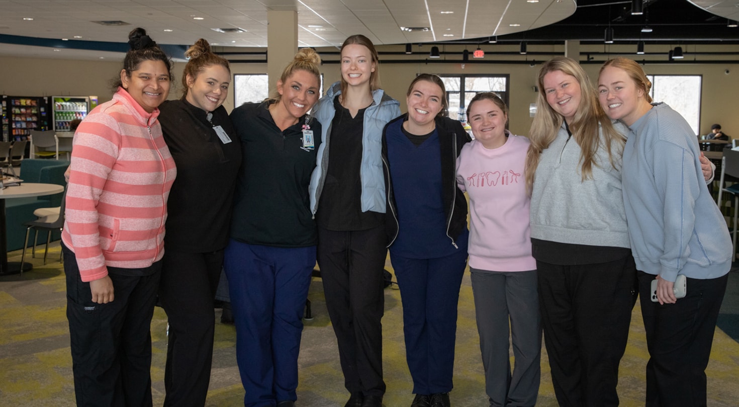 A group of students from the Dental Hygiene program standing in the commons, smiling at the camera.