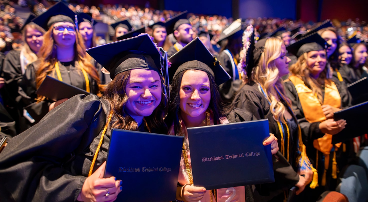 Two graduates smiling holding diplomas