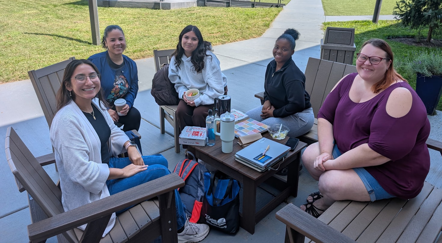 Students sitting at a table in the courtyard smiling at the camera