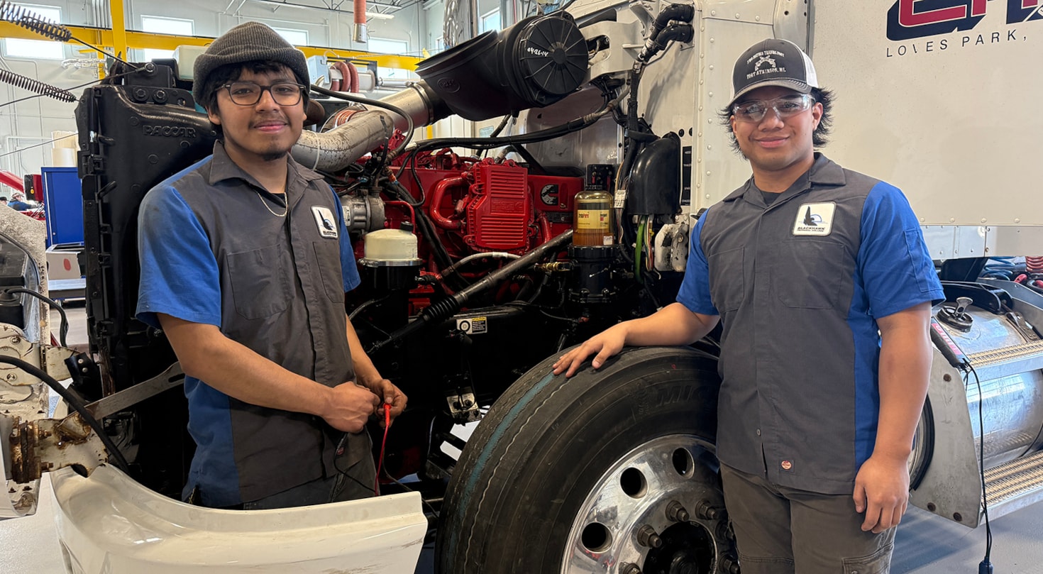 Two automotive students in front of a semi cab smiling at the camera