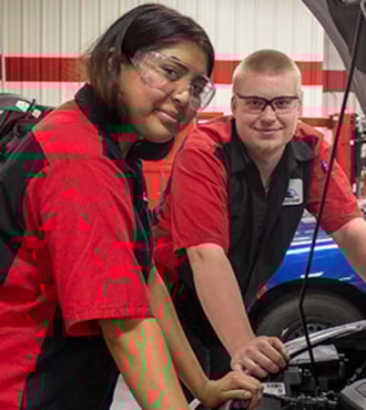 Automotive students standing with car hood open looking at camera