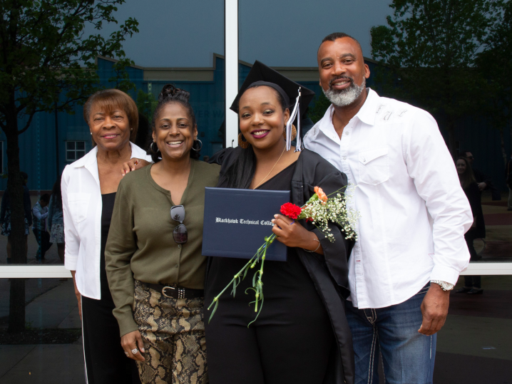 female graduate in cap and gown with diploma and family